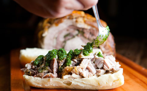 Sanduíche de porchetta, com carne suína em fatias, torresmo e molho de salsa